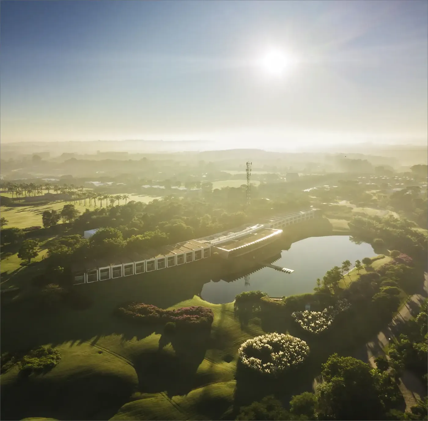Vista aérea da Fazenda Boa Vista com o sol baixo sobre os lagos, os jardins e a mata