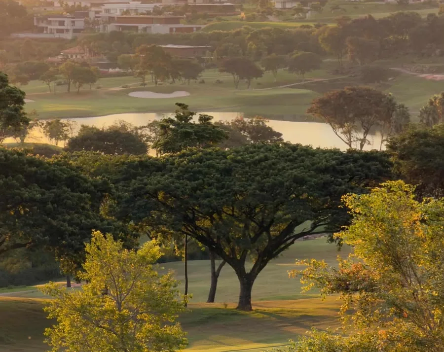 Campo de golfe da Fazenda da Grama ao entardecer, com o lago e as árvores iluminadas pelo sol