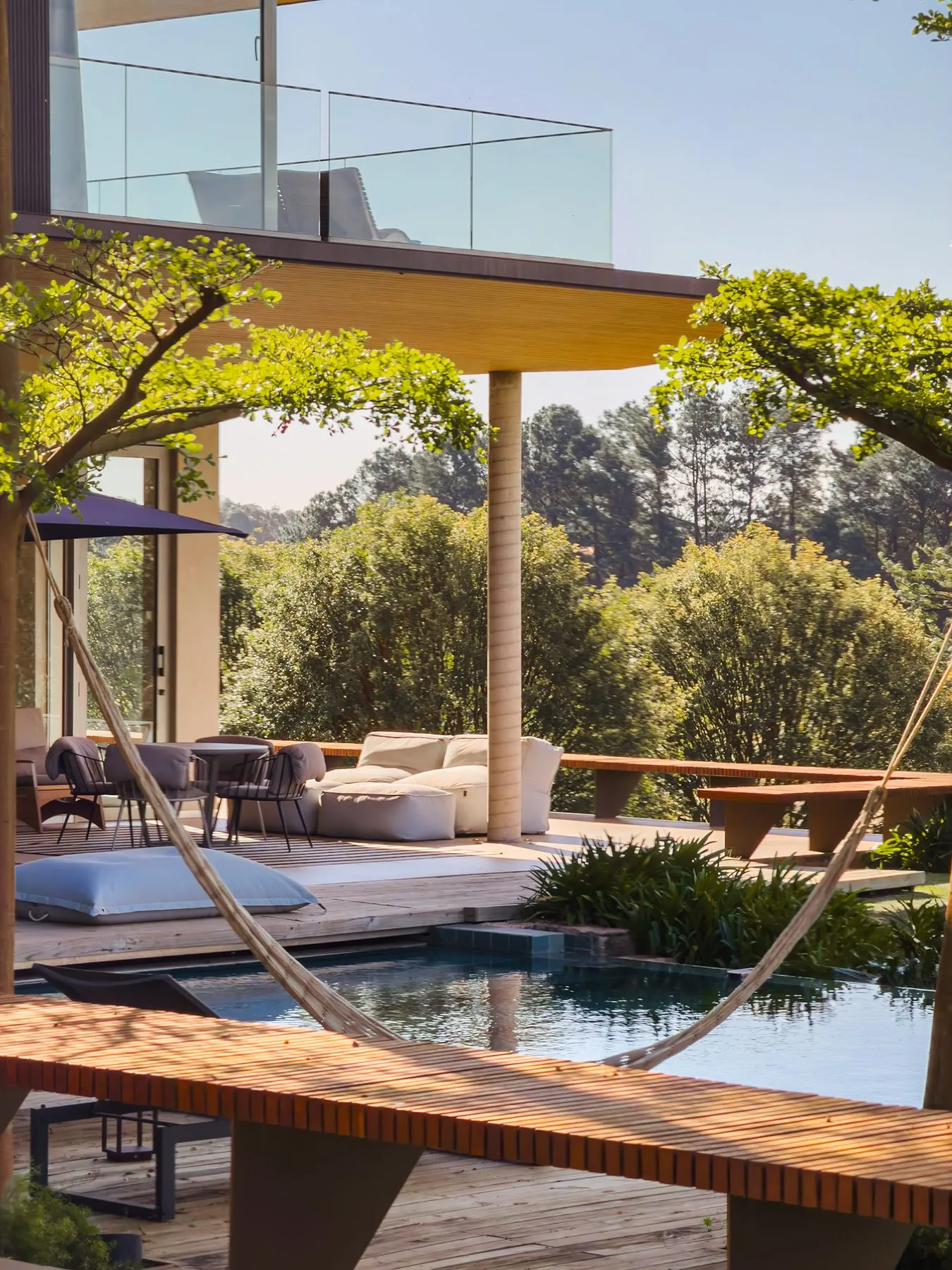Varanda coberta com sofás e pufes, aberta para as árvores
