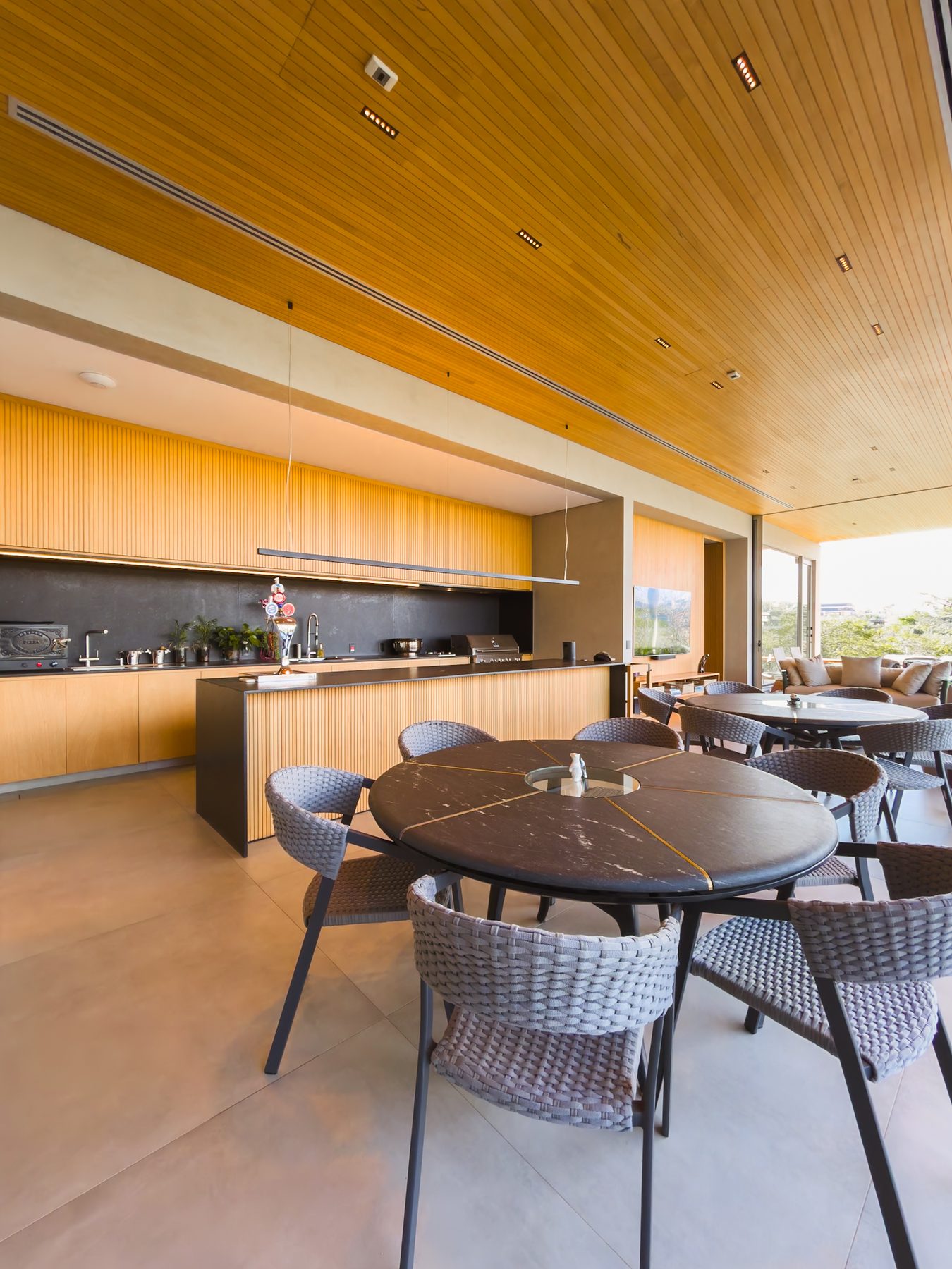 Espaço gourmet sob forro de madeira, com cozinha, mesa redonda e vista para o jardim