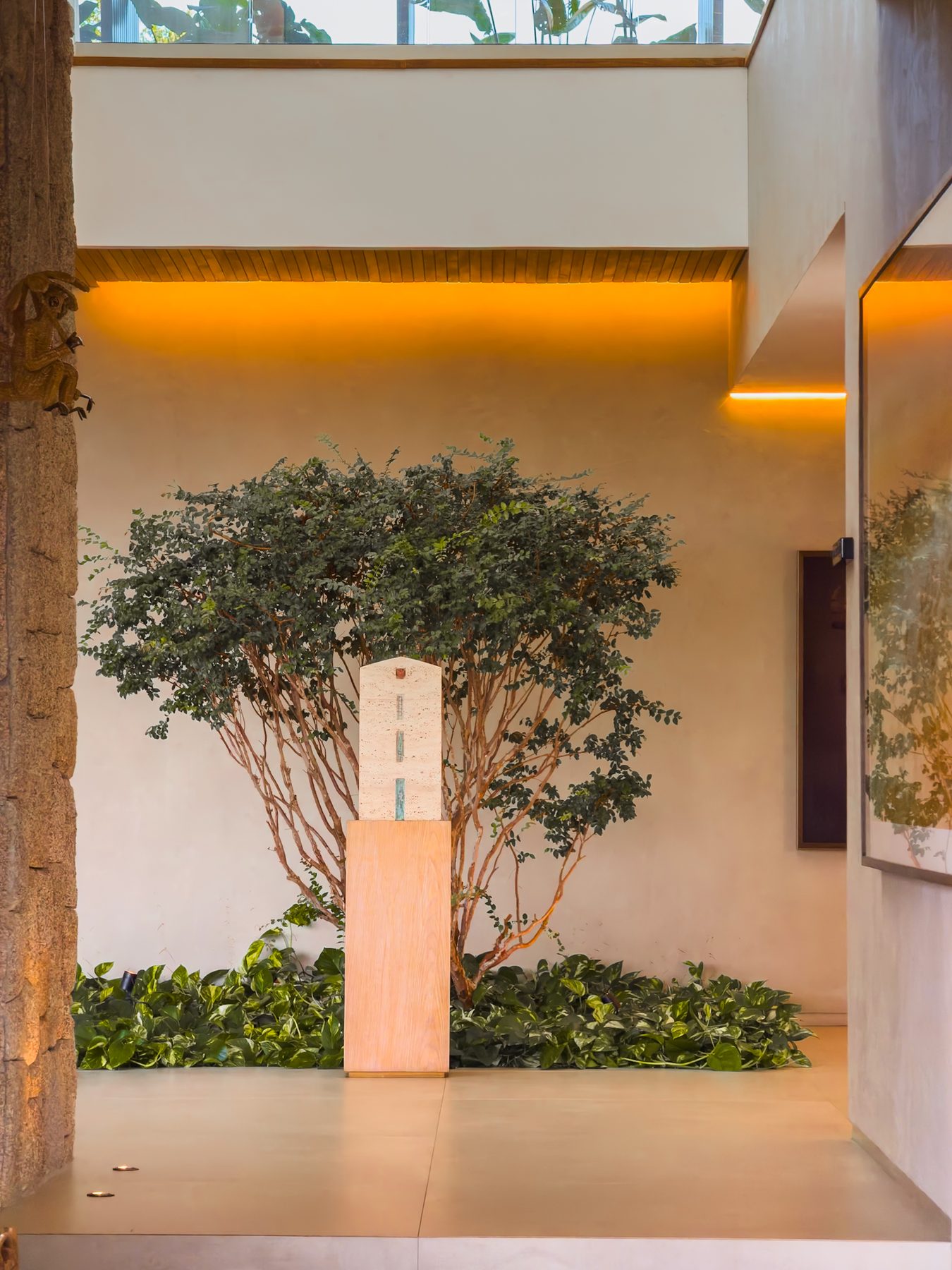 Árvore plantada em jardim interno, iluminada por abertura zenital e sanca de luz