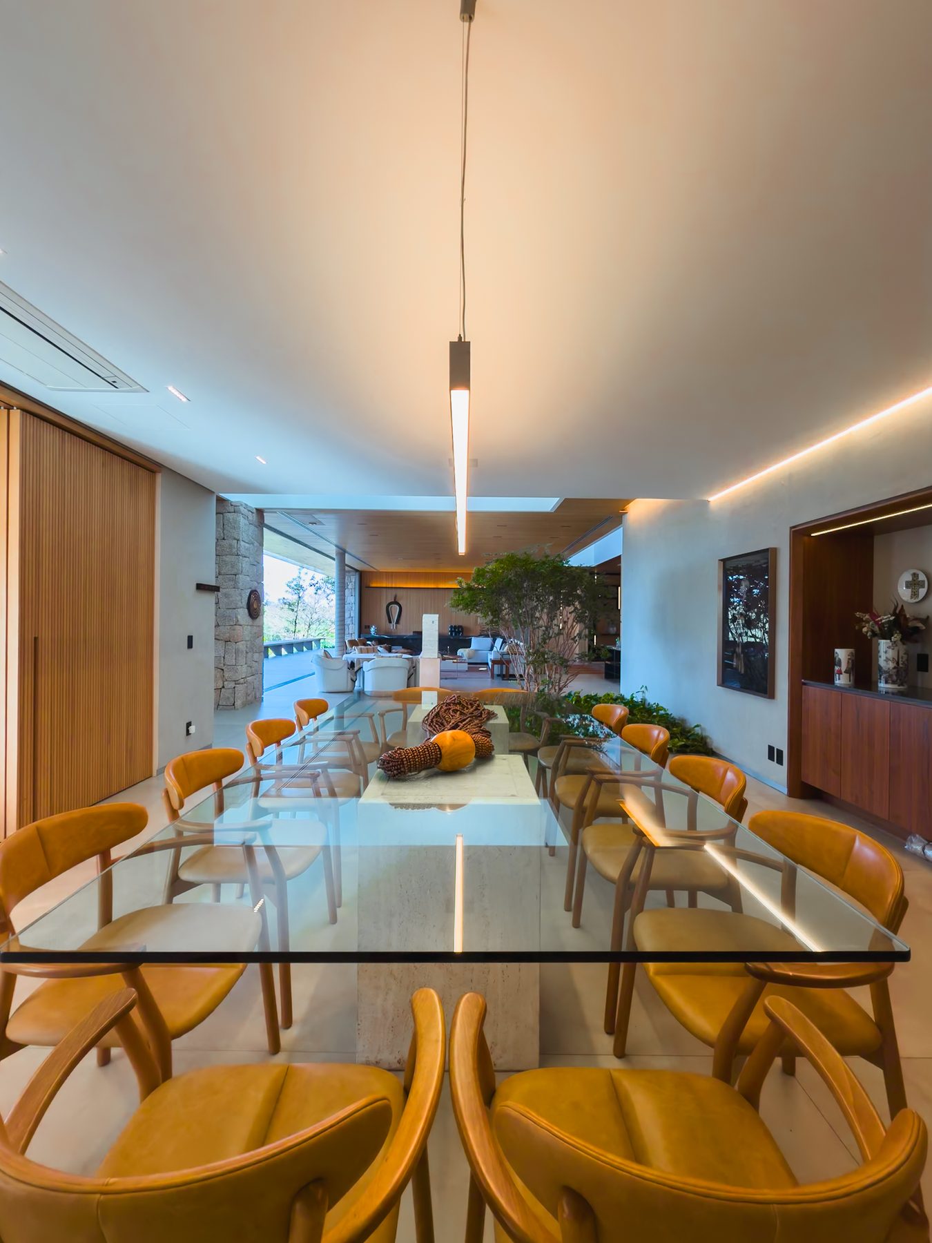 Sala de jantar com mesa longa de vidro e cadeiras de madeira, com o jardim interno ao fundo