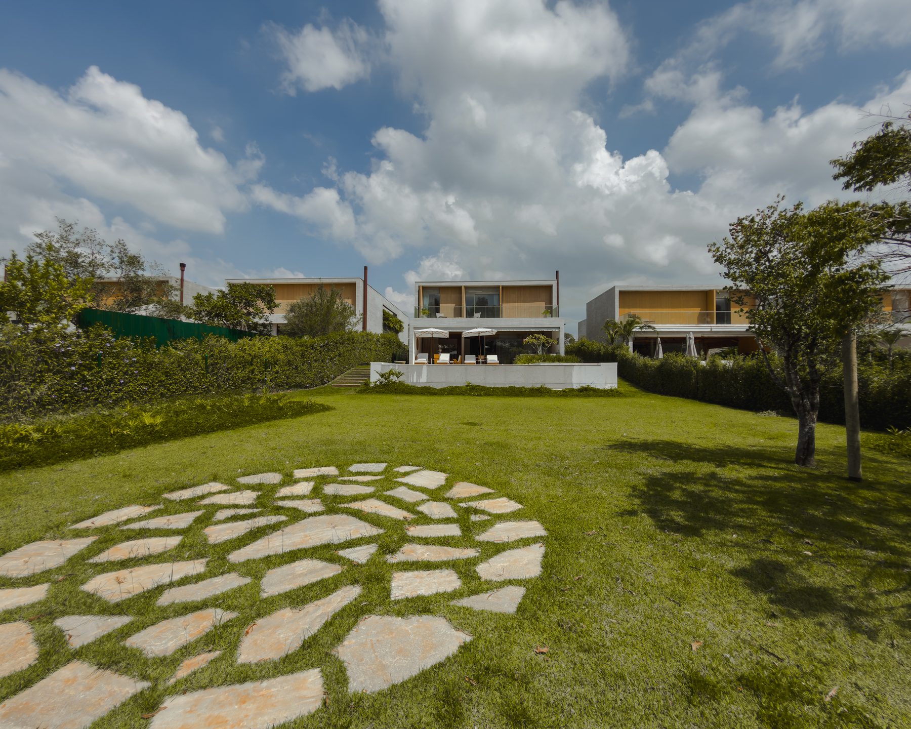 Gramado amplo com caminho circular de pedras, com a casa e a piscina ao fundo