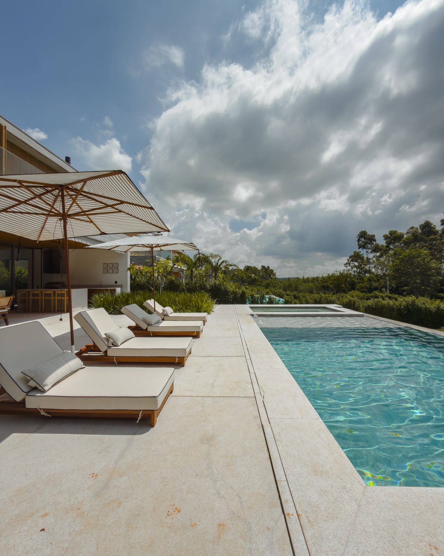 Deck com espreguiçadeiras ao longo da piscina, sob céu com nuvens