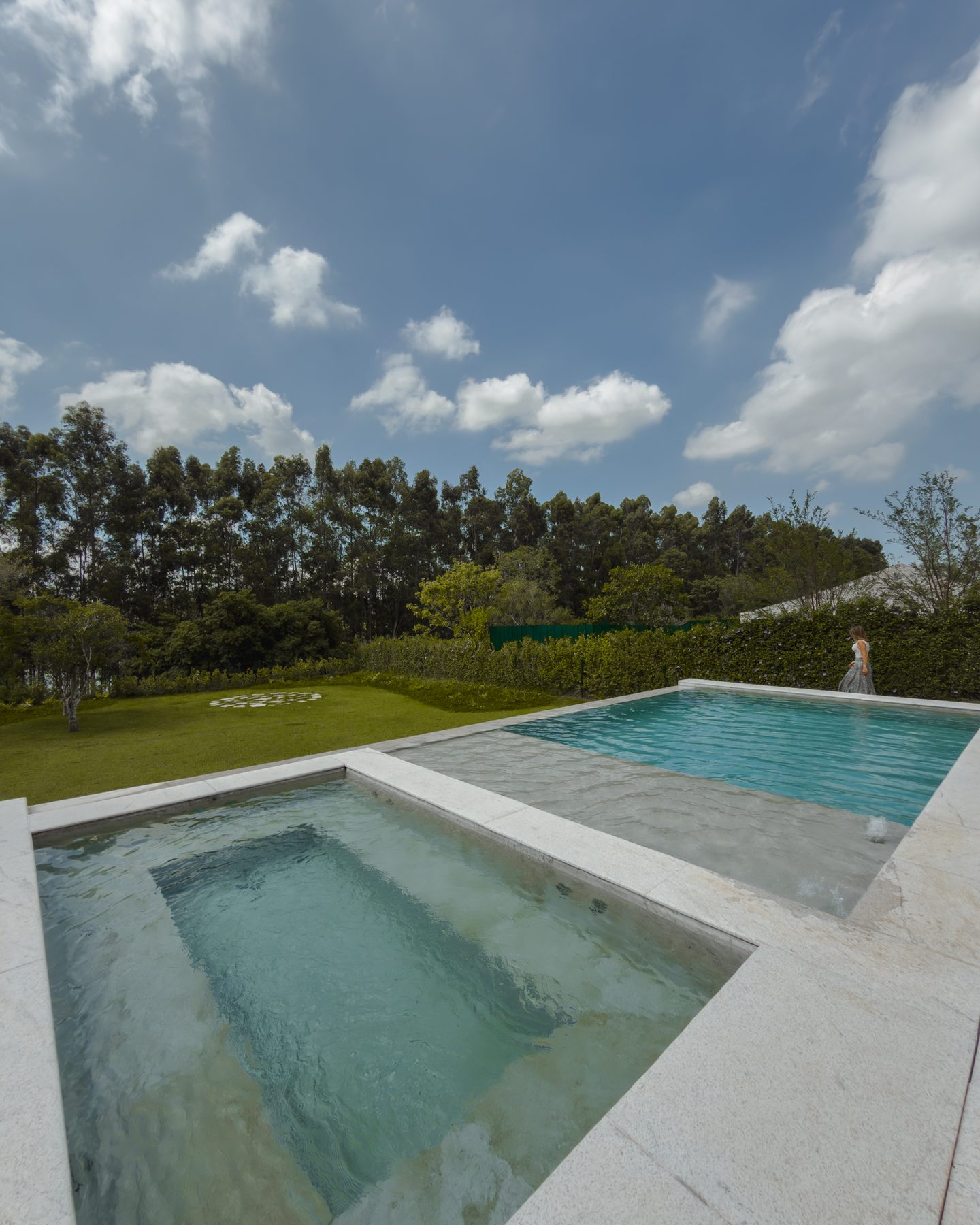 Área rasa de água ao lado da piscina, com o gramado e a mata ao fundo
