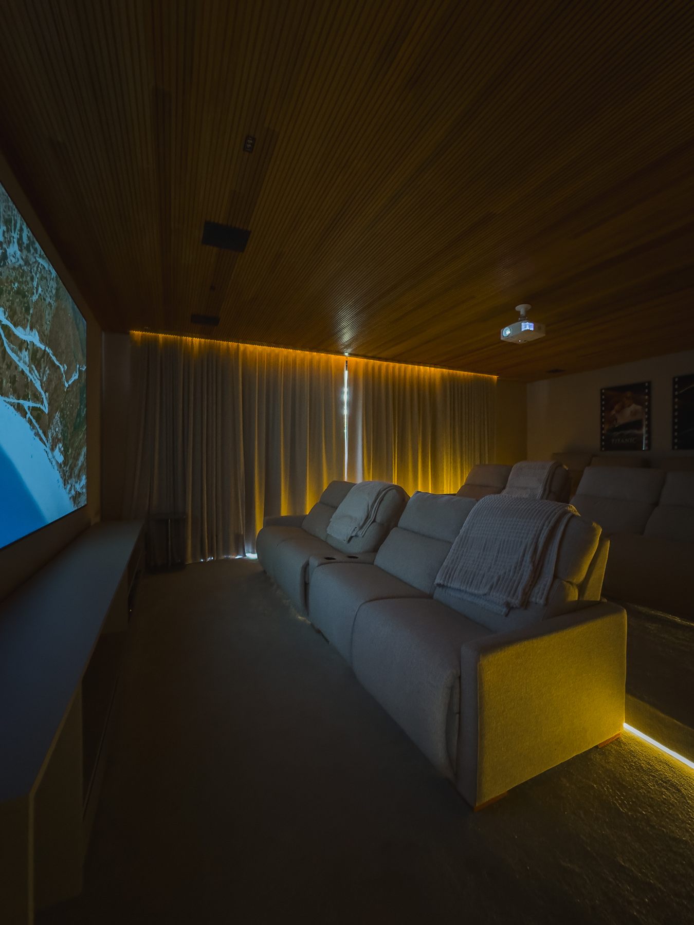 Sala de cinema com poltronas reclináveis, tela e forro de madeira com iluminação indireta