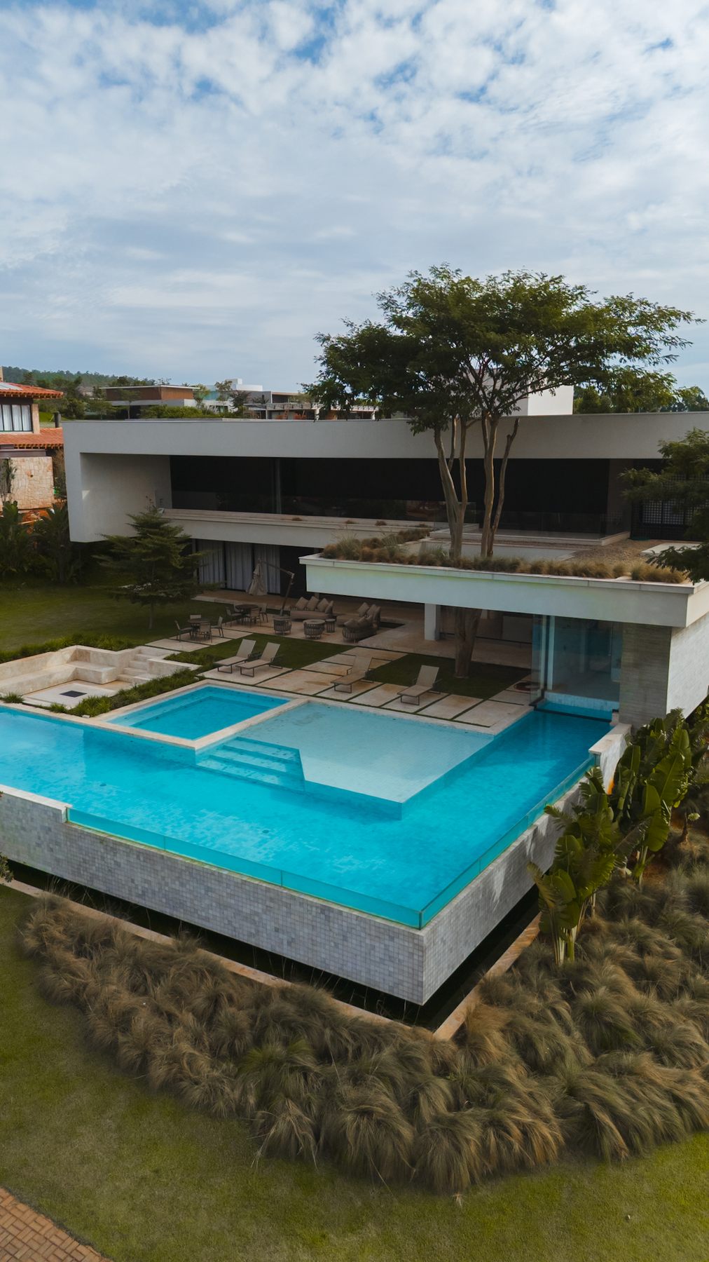 Vista aérea da piscina e da casa branca de dois pavimentos, com uma árvore sobre o terraço