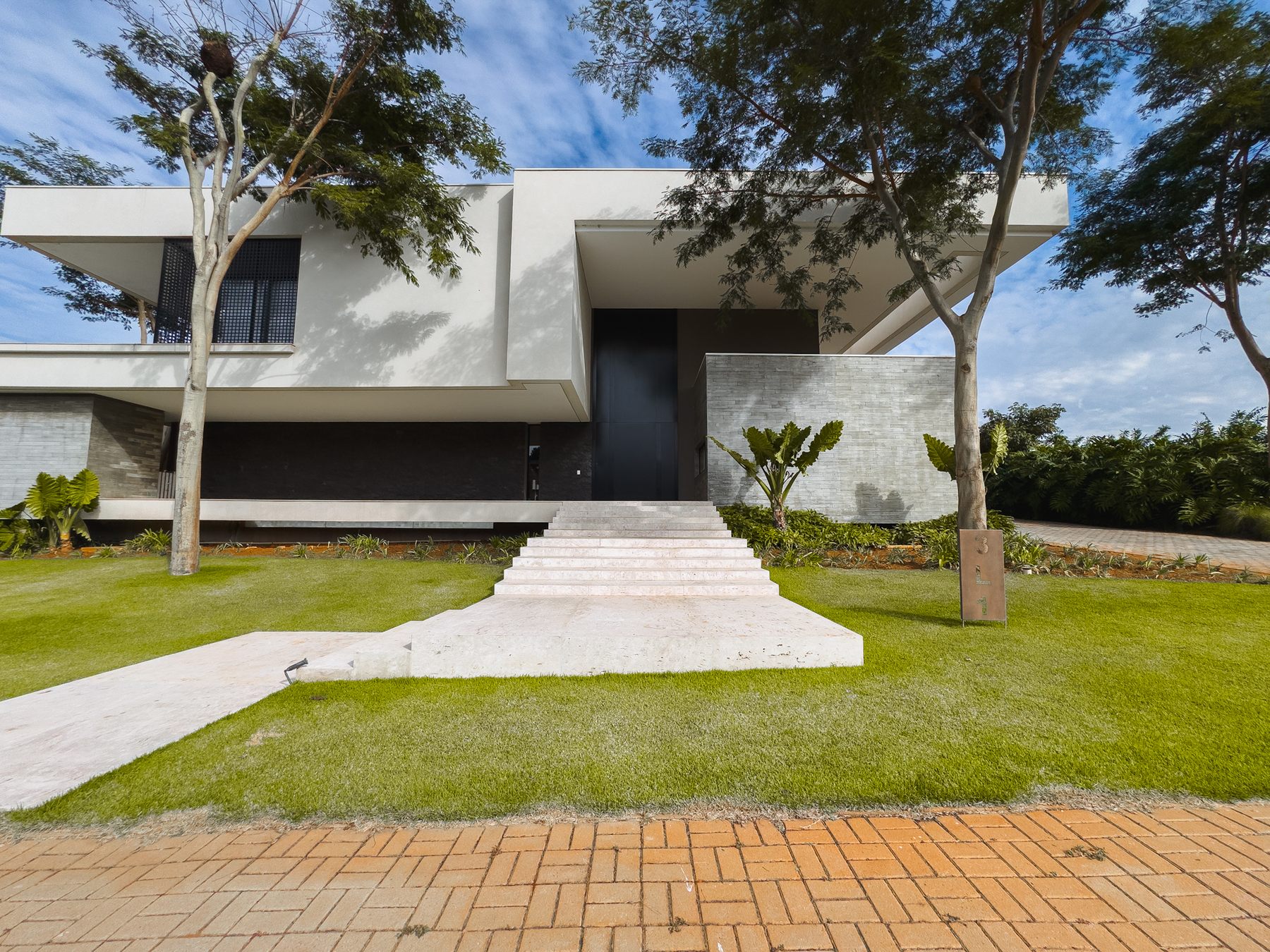 Fachada da casa com volumes brancos em balanço, parede de pedra e escada de pedra no gramado