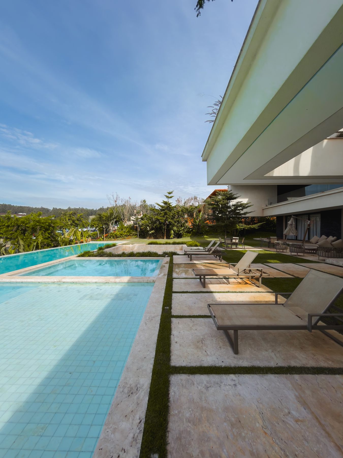 Piscina com espreguiçadeiras no deck de pedra, sob o balanço da casa branca