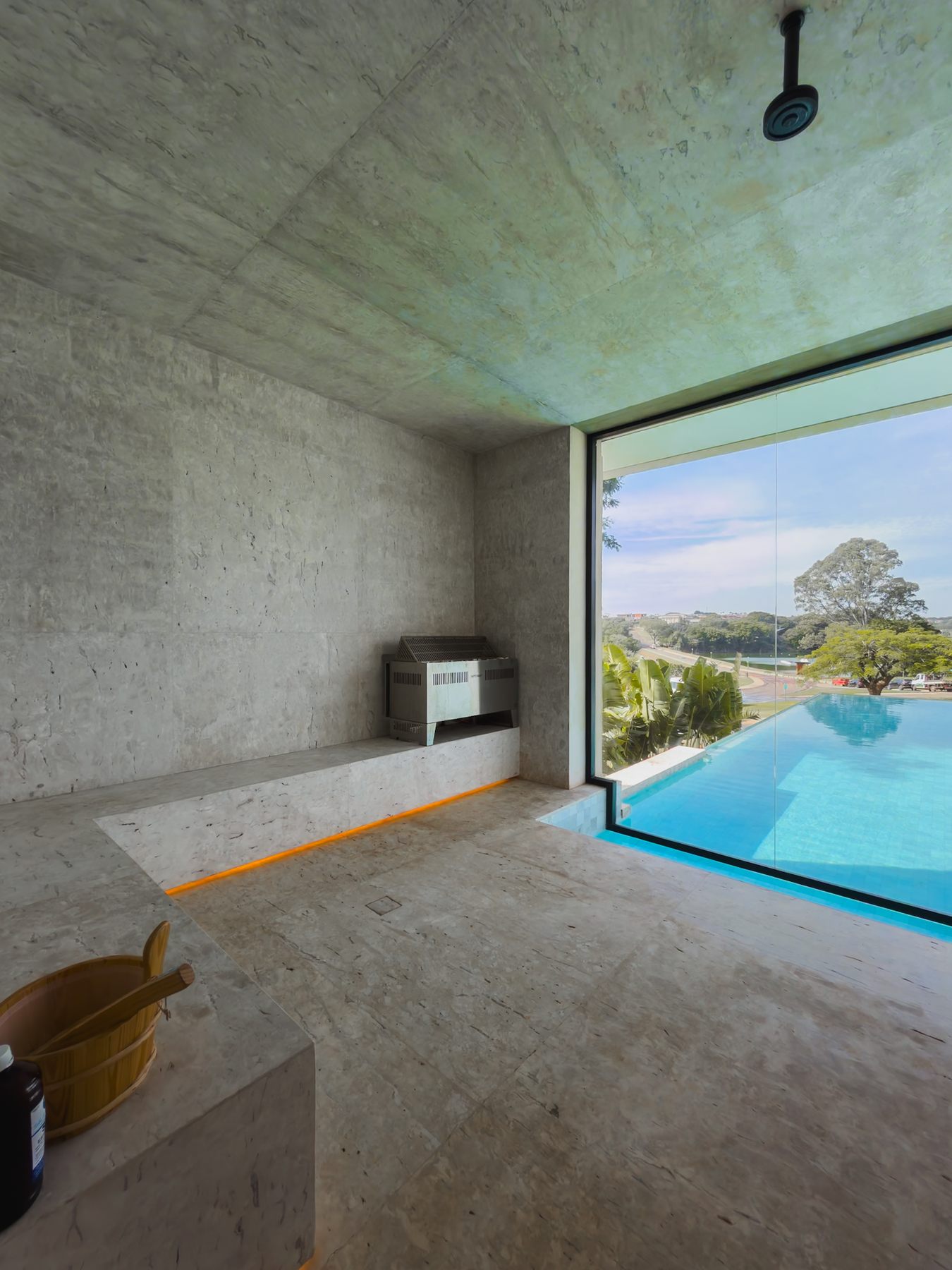 Sauna revestida em pedra, com bancos, balde de madeira e janela de vidro para a piscina