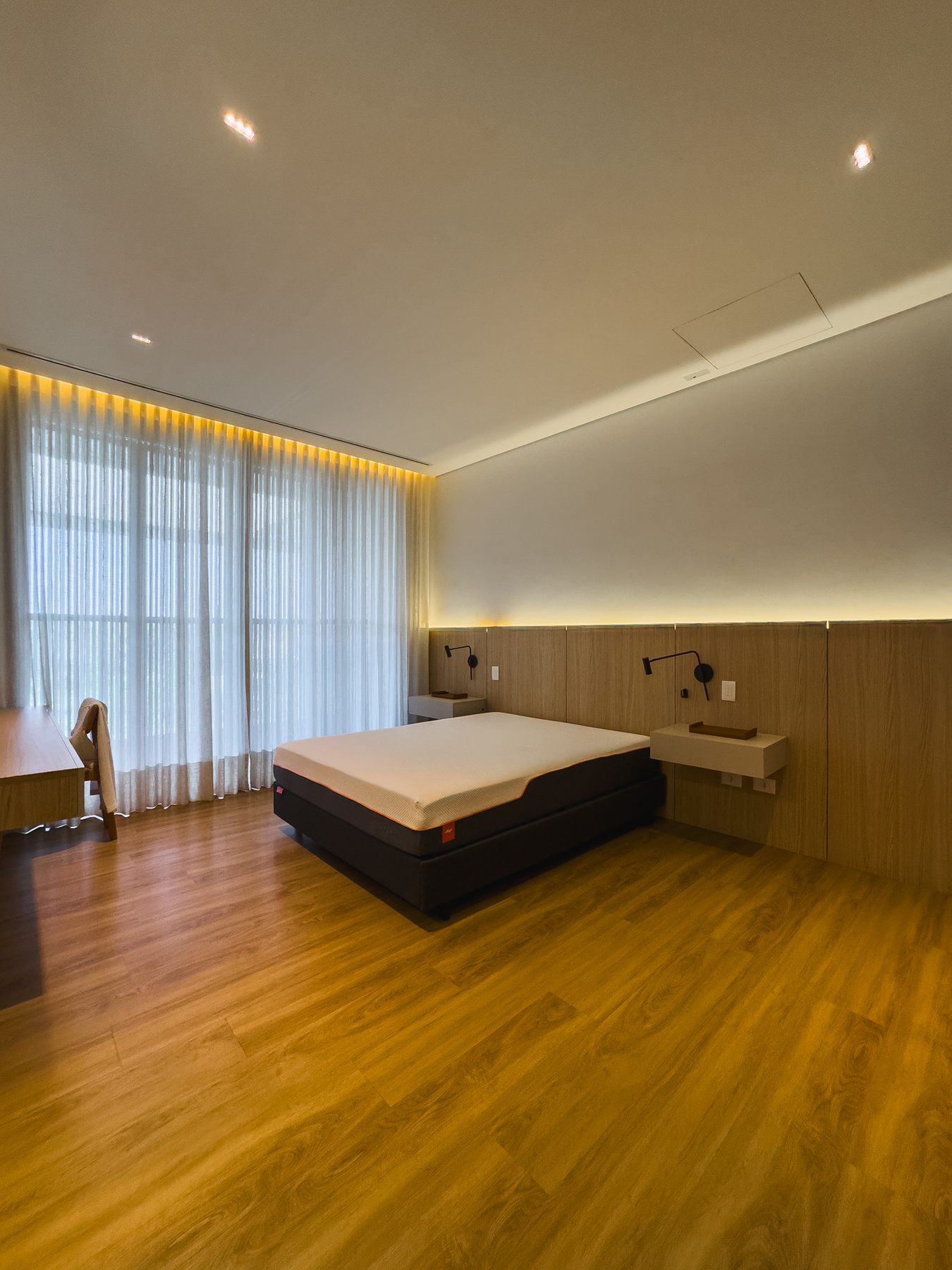 Suíte com cama de casal, painel de madeira e cortinas claras
