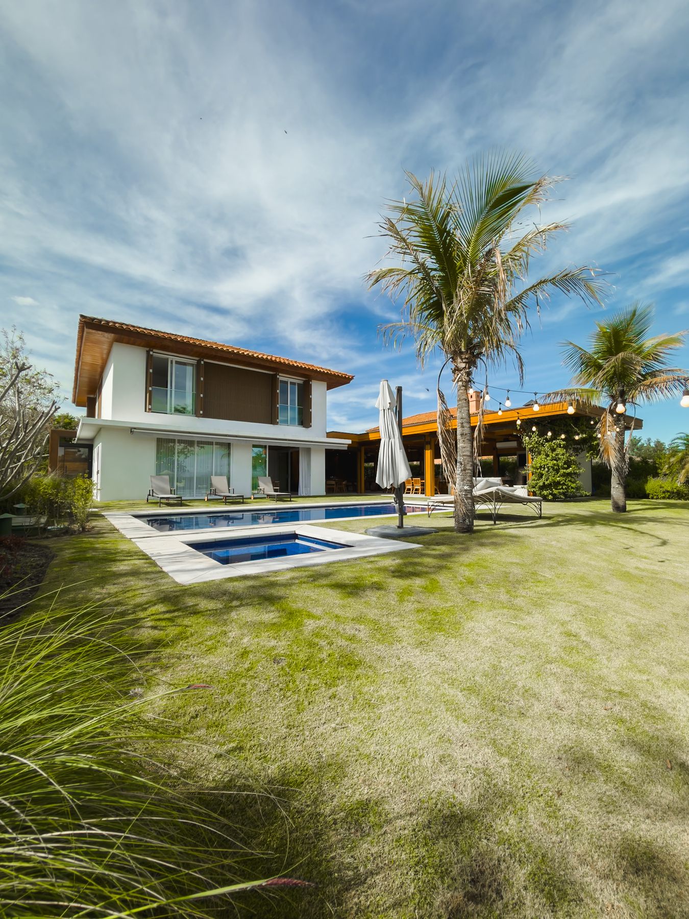 A casa de dois pavimentos com a piscina e uma palmeira no gramado, sob céu azul