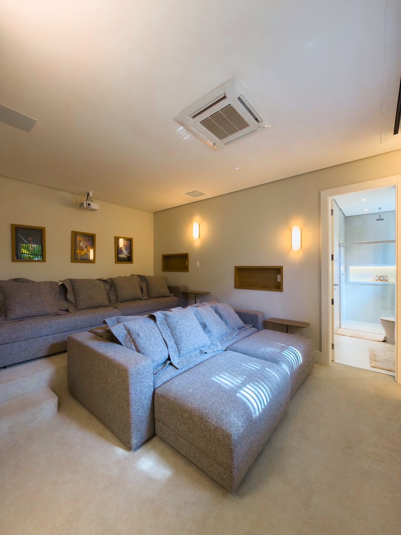 Home theater com sofá de módulos, projetor no teto e quadros na parede