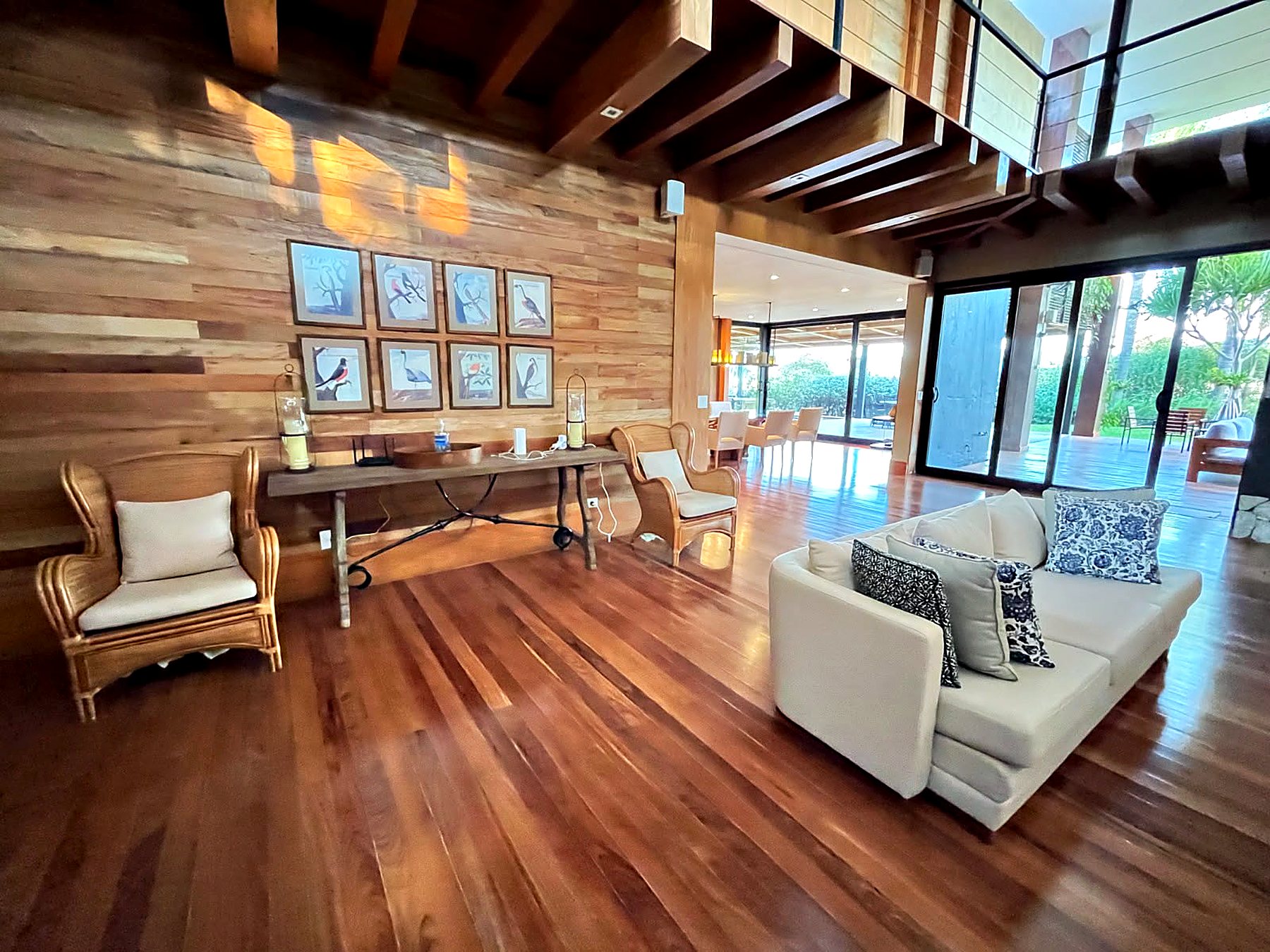 Estar com poltronas de palha, sofá claro e quadros de pássaros na parede de madeira