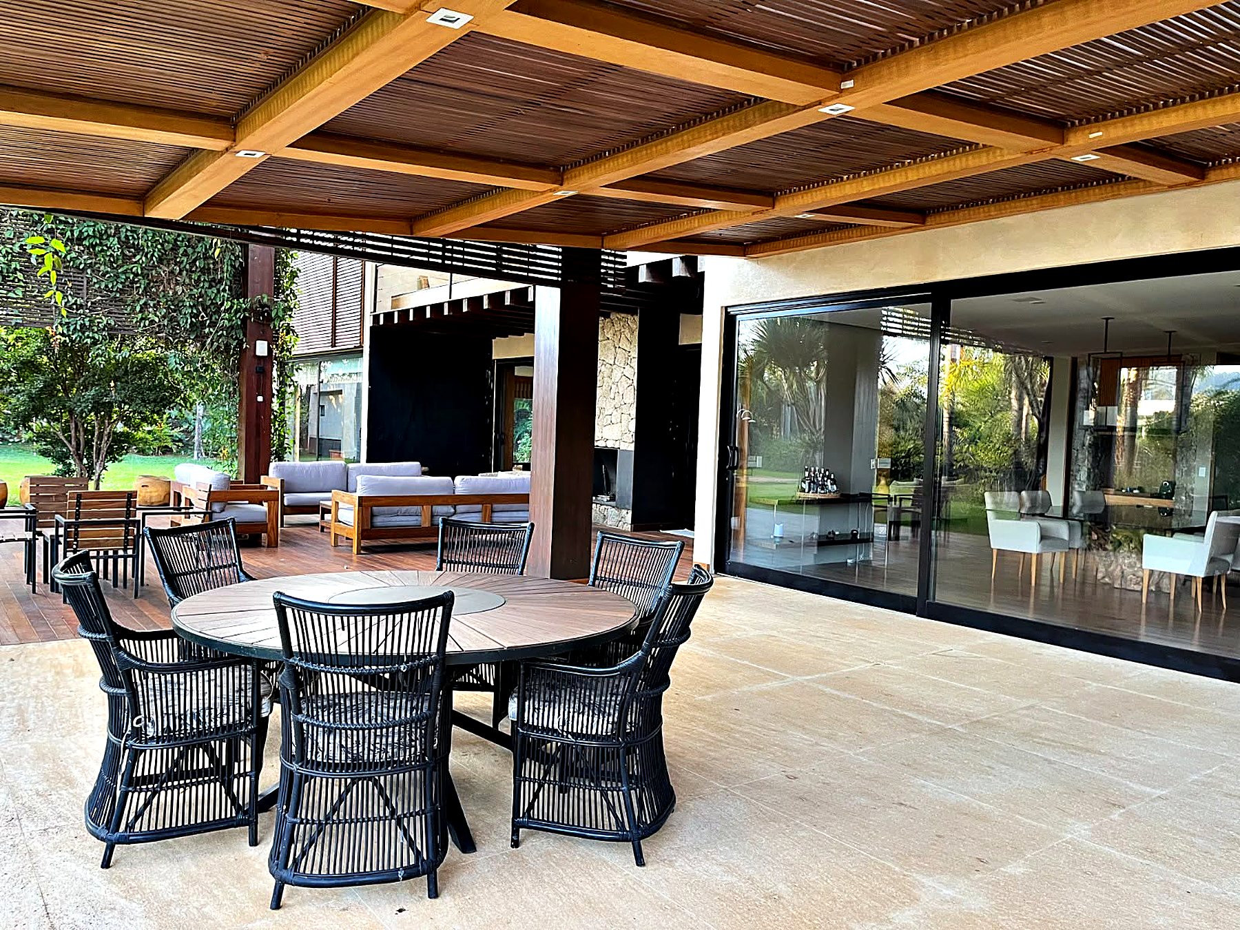 Terraço com mesa redonda e cadeiras escuras, aberto para o jardim e para o deck