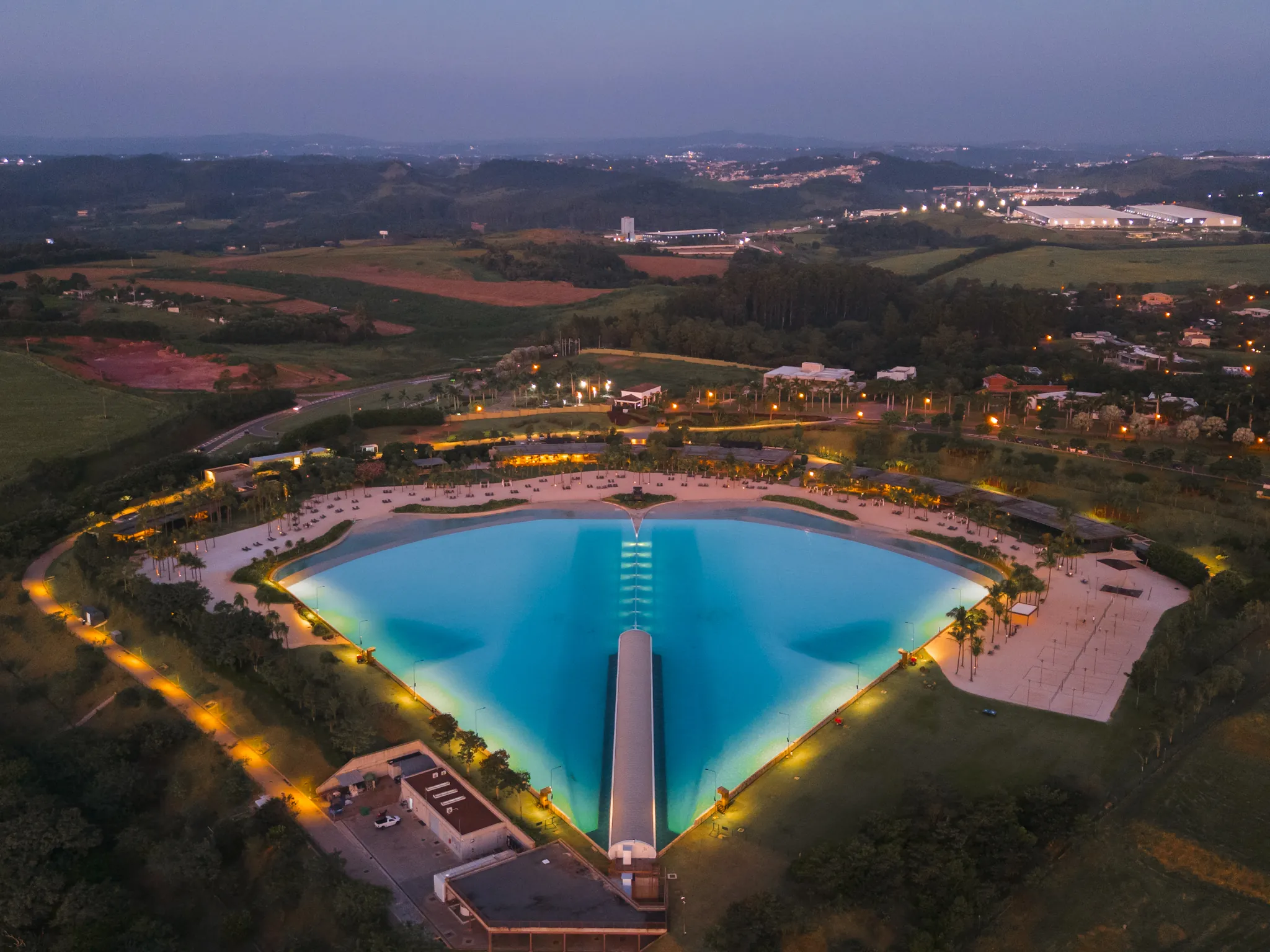 Vista aérea da Praia da Grama ao anoitecer, com a lagoa de ondas iluminada, a faixa de areia e as palmeiras